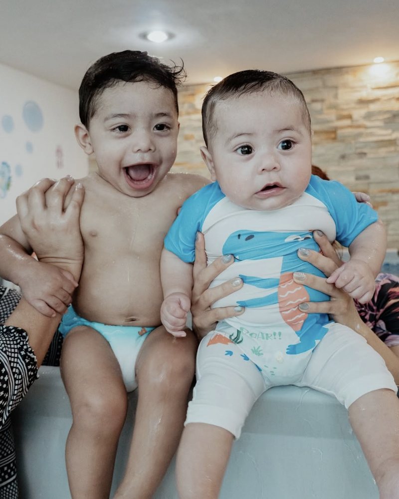 Dos bebés felices sentados en la orilla de la alberca de Olita de Mar